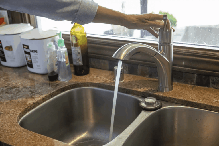 A hand turning on a kitchen faucet